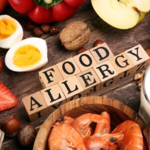 'Food allergy' spelt out in wooden blocks in the middle of display of food including eggs, strawberries, apple, carrots, prawns and milk