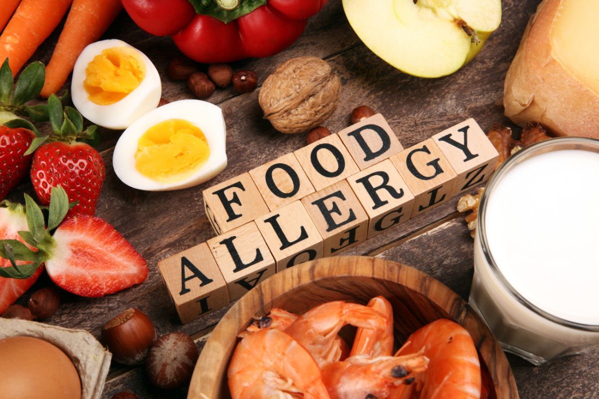 'Food allergy' spelt out in wooden blocks in the middle of display of food including eggs, strawberries, apple, carrots, prawns and milk