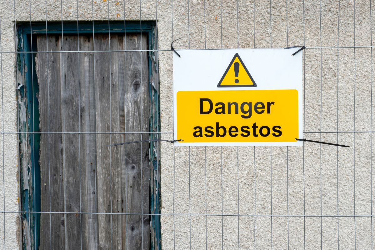 Railings outside a building with a large warning sign saying Danger asbestos pinned to it