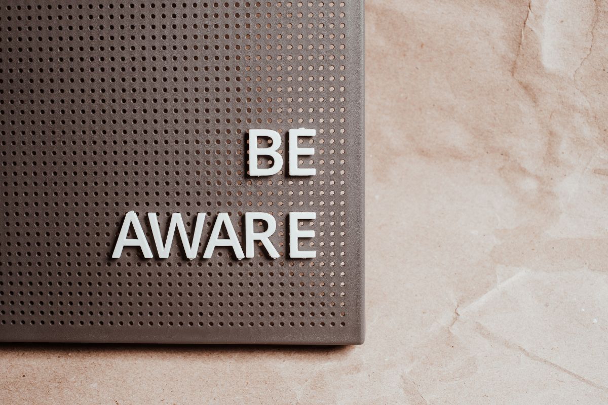 A black pinboard on a light background with letters pinned in spelling out BE AWARE