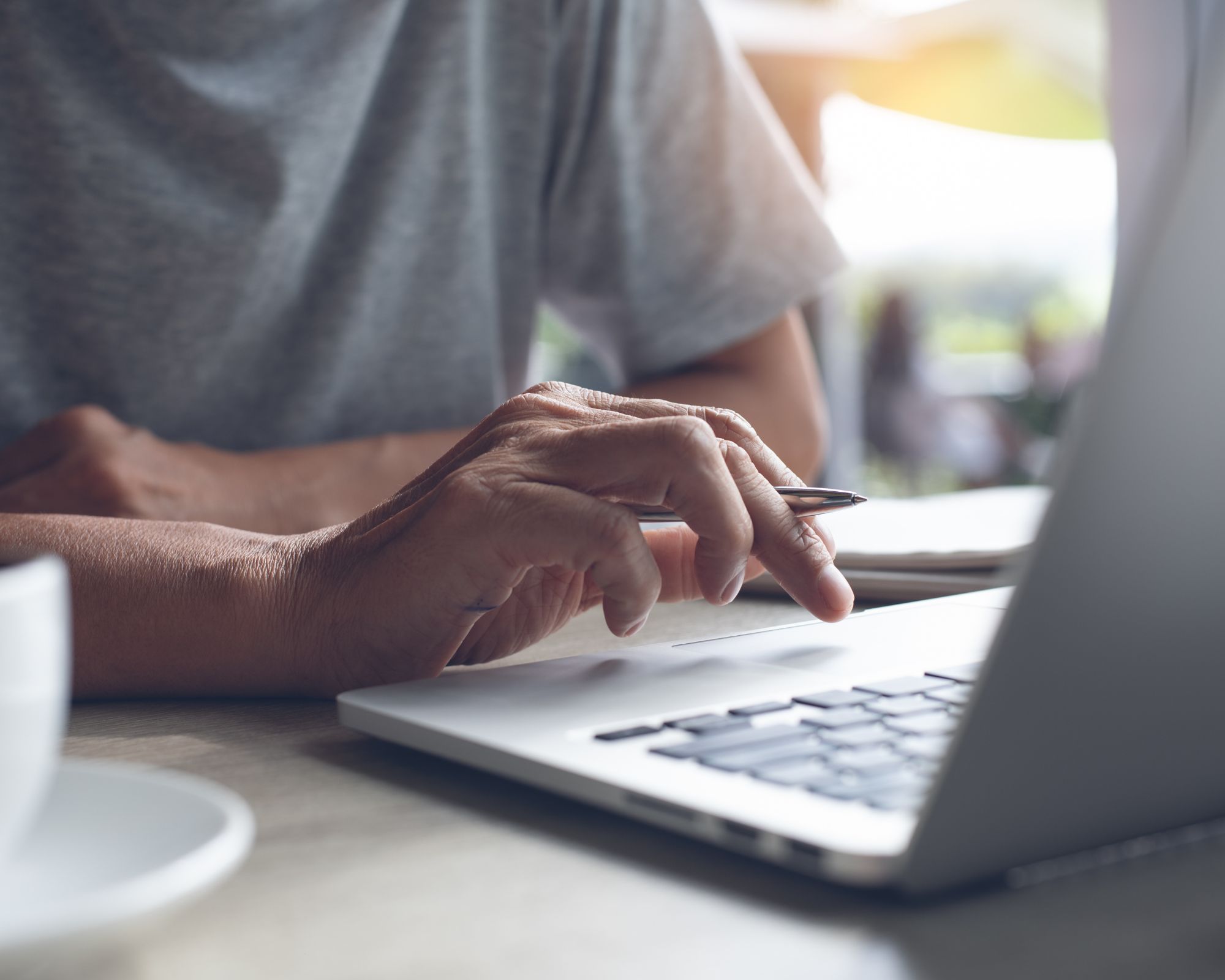 Close up image showing someone and their hand holding a pen and hovering over a laptop keyboard