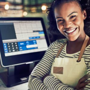 A smiling worker with apron on and arms folded in front of a till screen