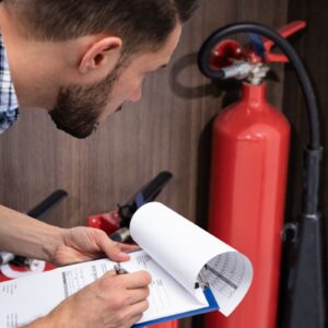 Inspector inspecting fire safety equipment and fire extinguisher with clipboard and paperwork