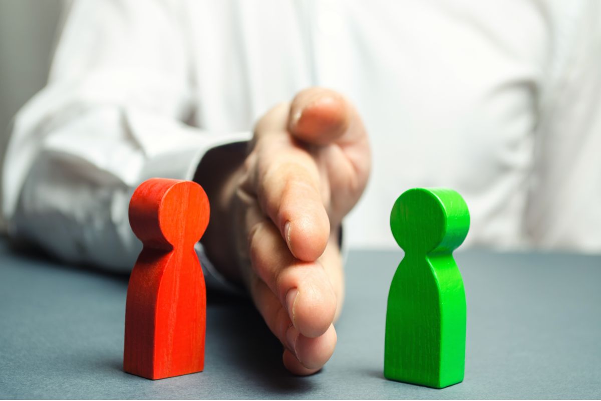 Image showing a red and green wooden 'person' on a table with a real persons hand on a table separating them