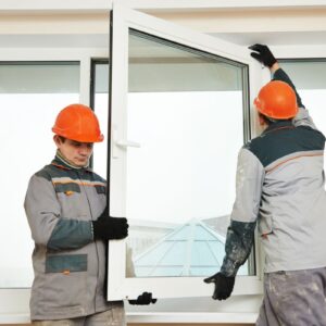 Two workers pictured in front of a large window manual handling the middle pane and trying to fix it in place
