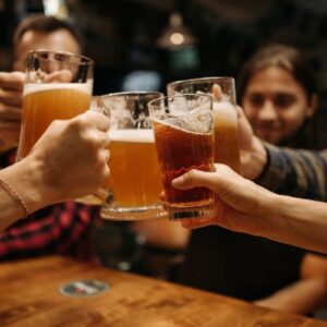 Image showing five pints of beer being 'cheered' in the centre, just showing three arms and two blurred faces behind