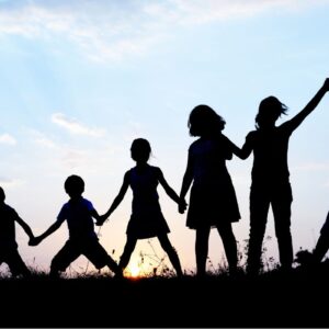 Image showing a shadowed line of seven children in a field holding hands from smallest to largest with the sun setting behind them