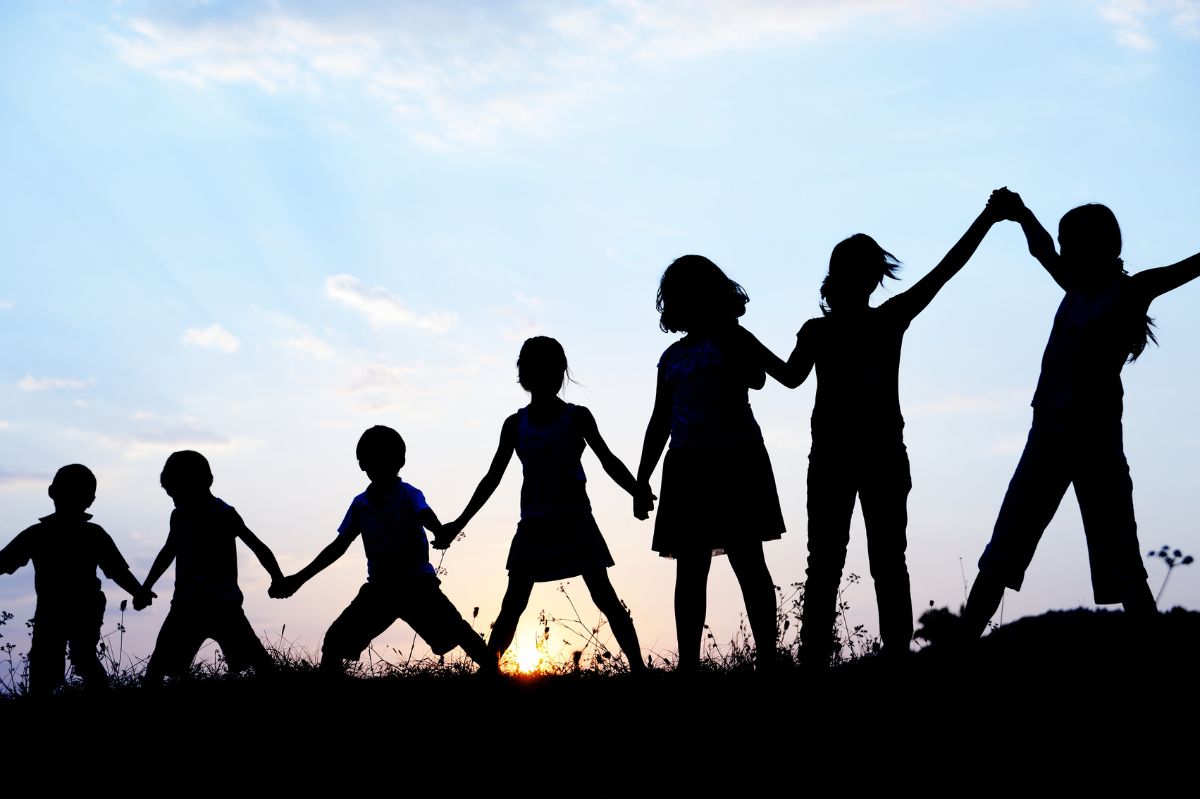 Image showing a shadowed line of seven children in a field holding hands from smallest to largest with the sun setting behind them