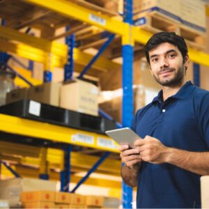 Worker holding a tablet with warehousing shelving and boxes behind him