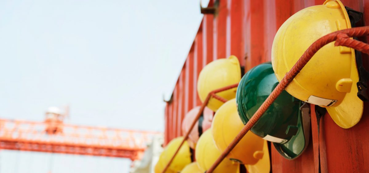 Image showing a building site container with a couple of rows of Health and Safety Helmets strapped to it and crane blurred in the background